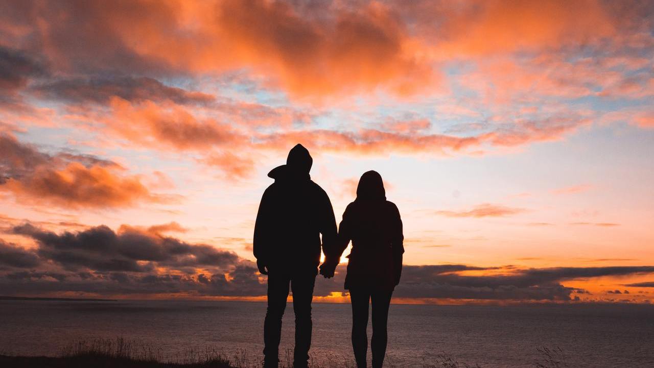 Couple holding hands in front of sunset with red sky